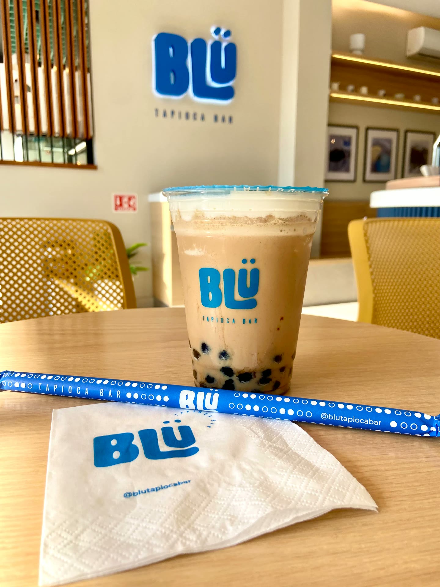 Latte con tapioca de BLÜ sobre mesa con servilleta y popote de la marca