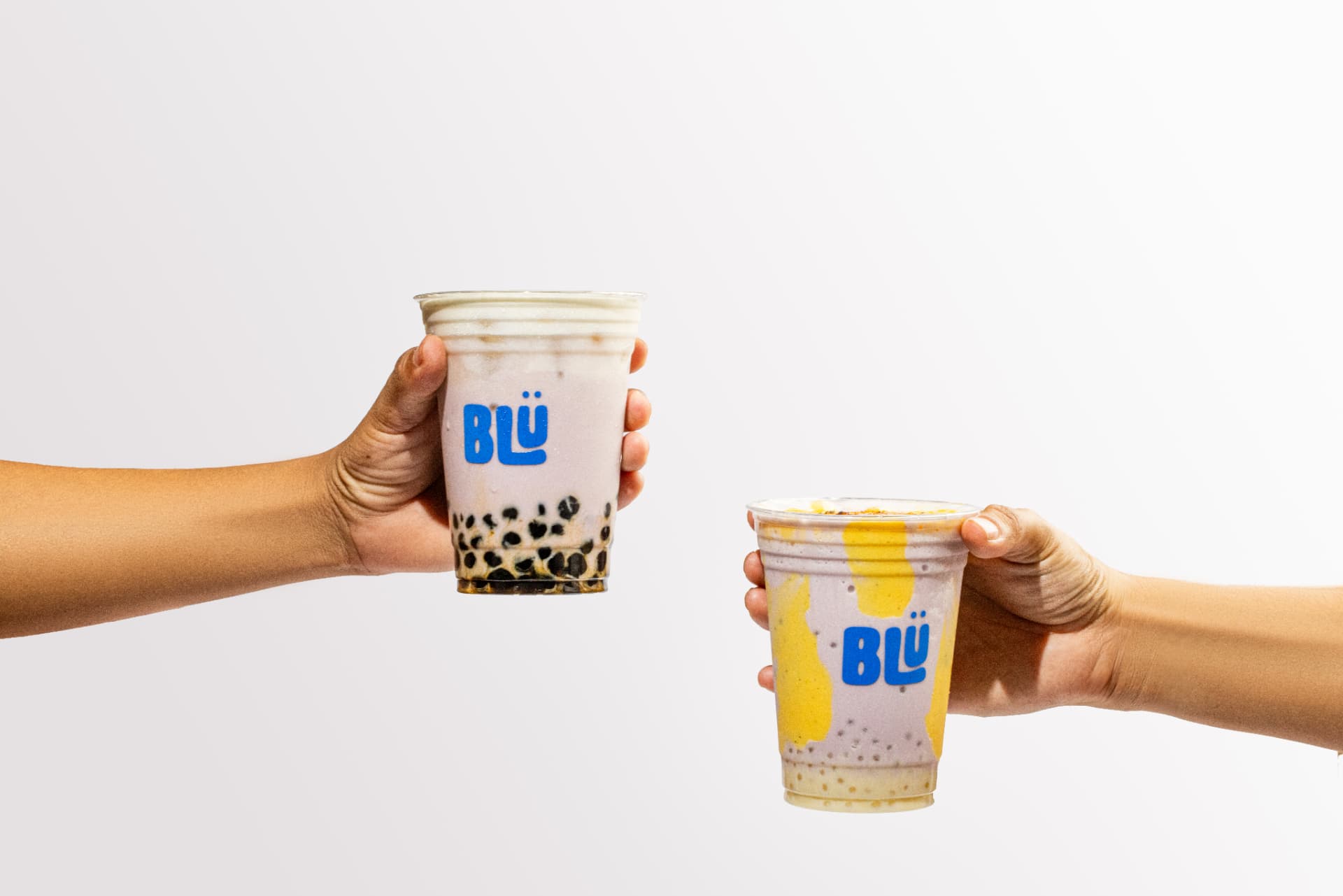 Dos manos brindando con bebidas de tapioca de BLÜ